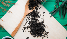 top-view-dry-black-tea-leaves-scattered-from-glass-jar-with-wooden-spoon-kitchen-cutting-board-green-wood.png